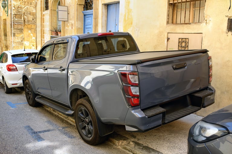 Pickup SUV with closed cargo bed parked on narrow street, rear angle view