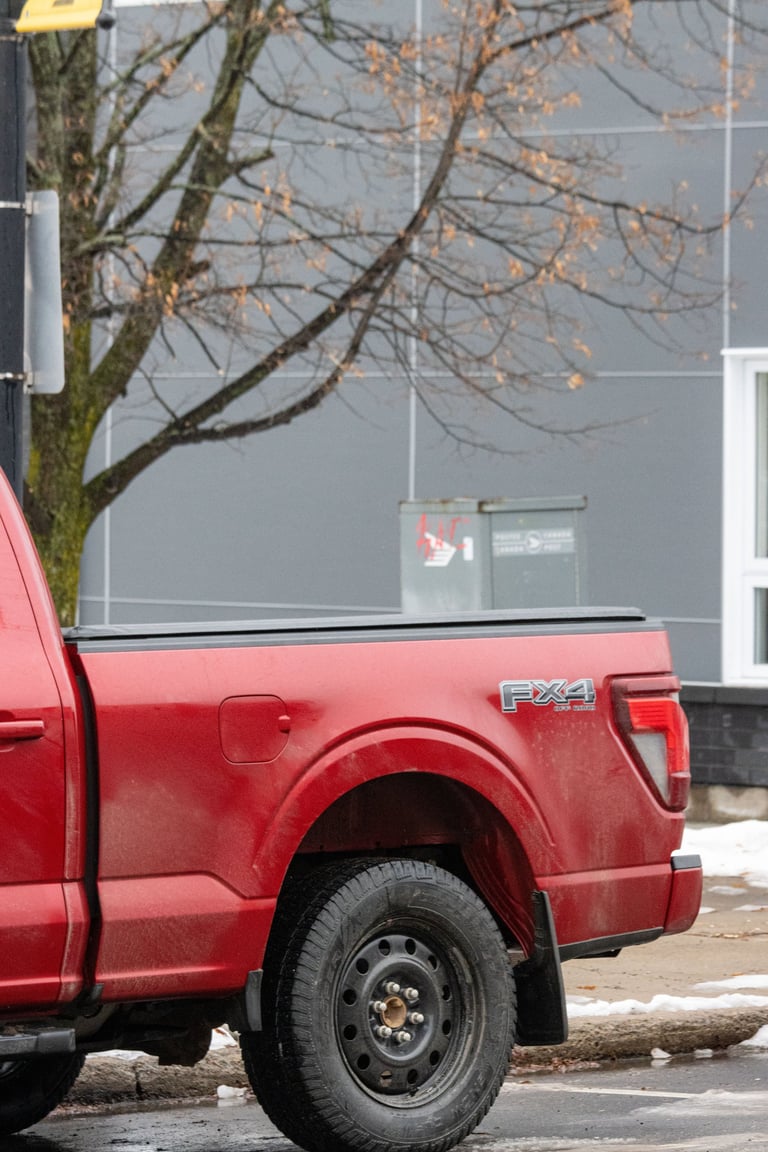 Red pickup truck parked near tree and contemporary building exterior sidewalk