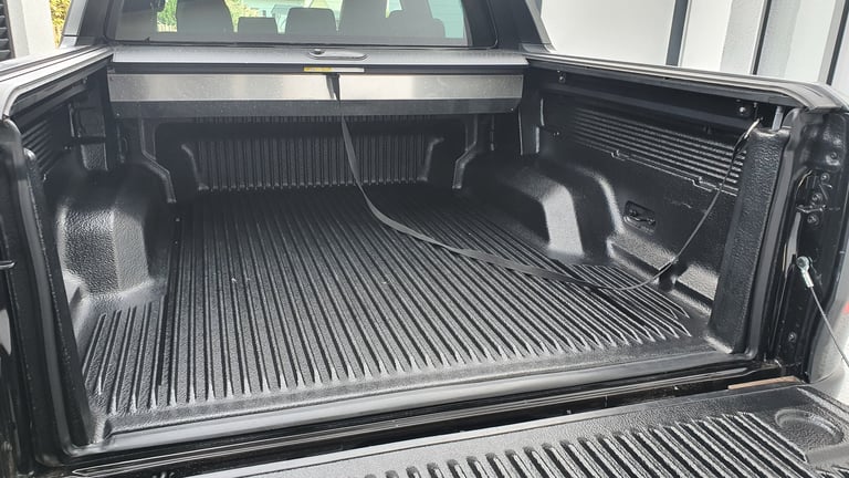 Interior of a modern pickup truck bed featuring a closed retractable cover and tie-down strap