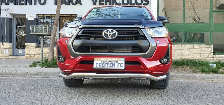 Red Toyota pickup truck parked on street with custom license plate and storefront in background