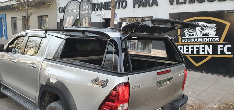 Silver pickup truck parked with open cargo bed door in front of a storefront with signage