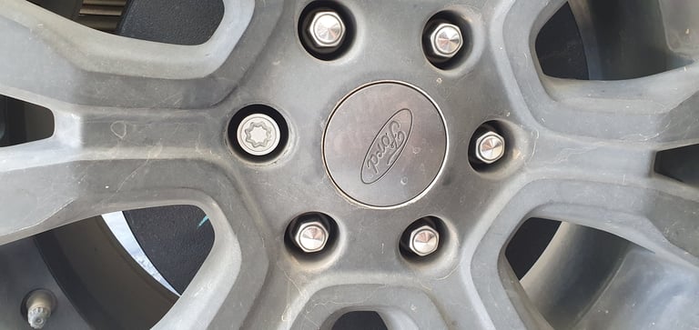 Close-up of a silver car wheel hub cap with lug nuts and center emblem visible