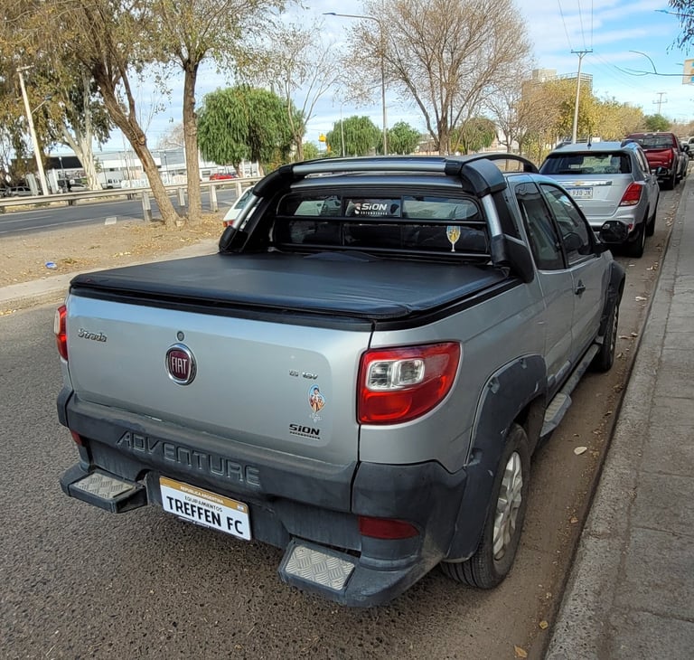 Silver Fiat pickup truck with tonneau cover parked on a street with trees in the background