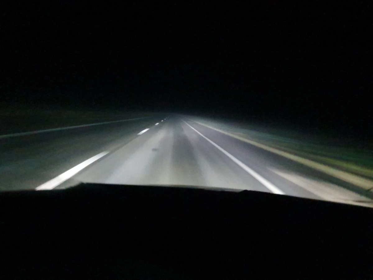 Night dashcam view of a straight highway with white lane markings stretching into darkness