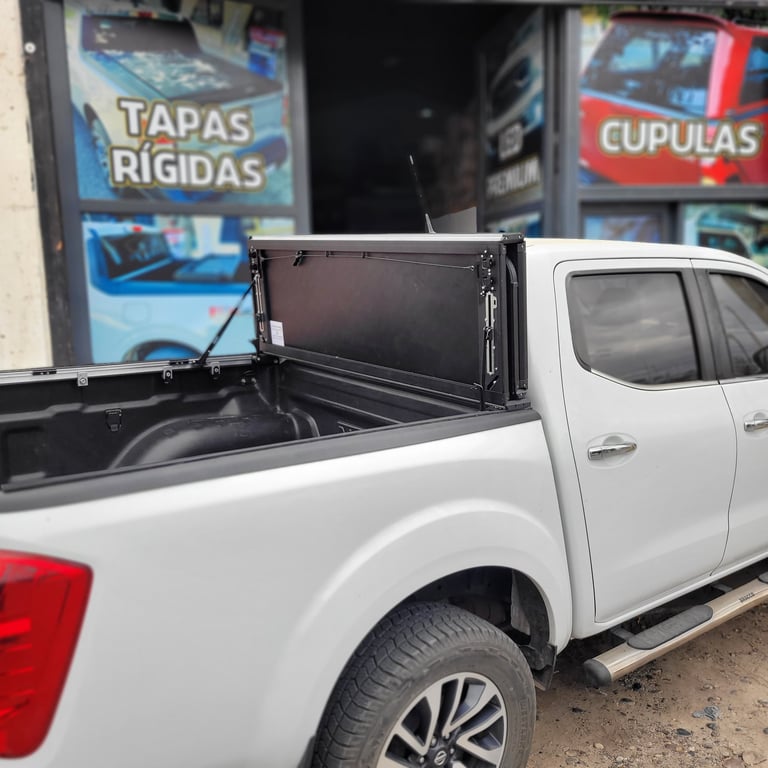 White pickup truck with open tonneau cover in bed, parked outside a shop with Spanish signage
