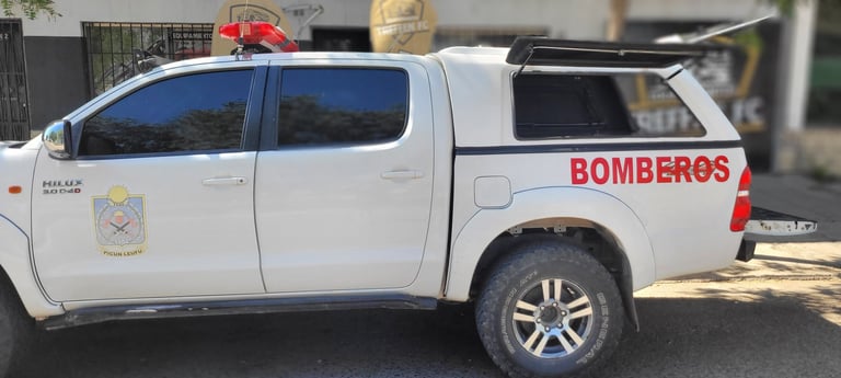 White pickup truck with red BOMBEROS lettering and emergency lights on roof, parked in outdoor lot