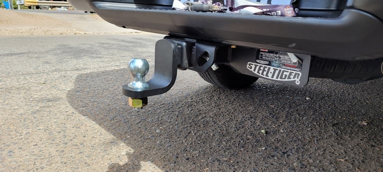 Close-up of a chrome tow hitch ball attached to a dark-colored vehicle bumper on pavement
