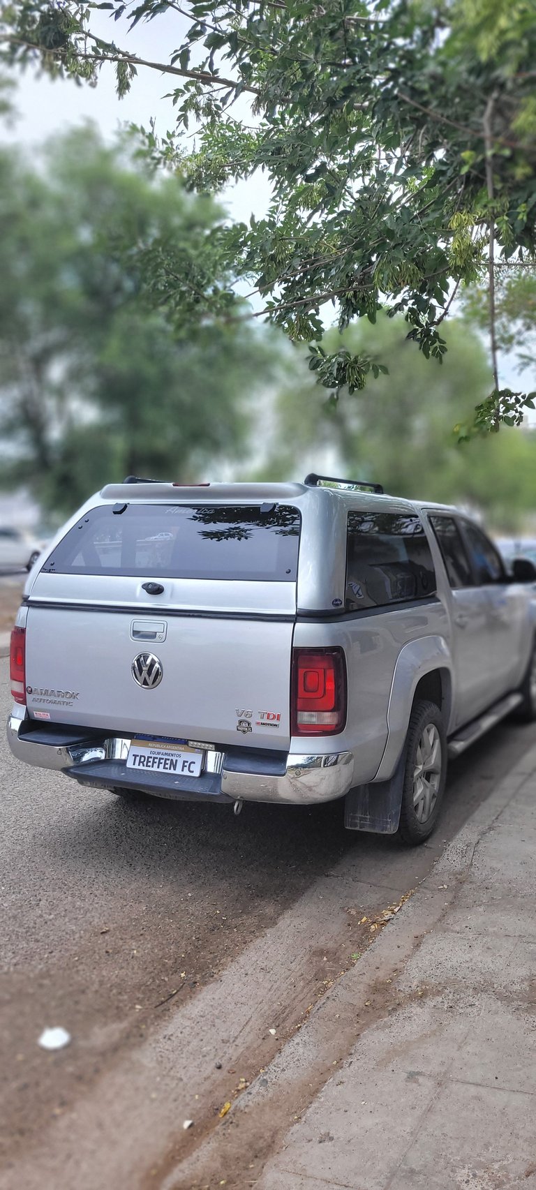 White Volkswagen pickup truck parked on a street lined with green trees