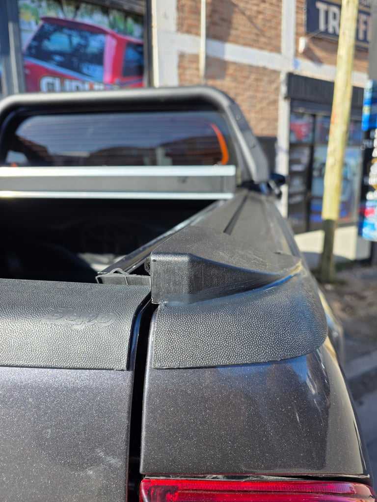 Close-up of a pickup truck bed cover and edge, with urban storefront visible in soft focus background