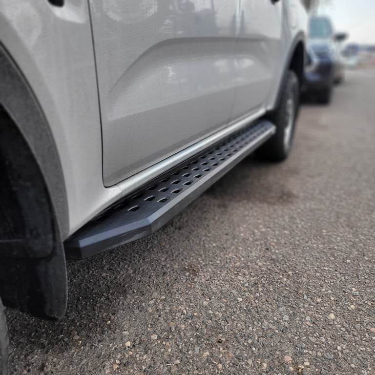Close-up side view of a white vehicle showing a black running board or step rail mounted below the door
