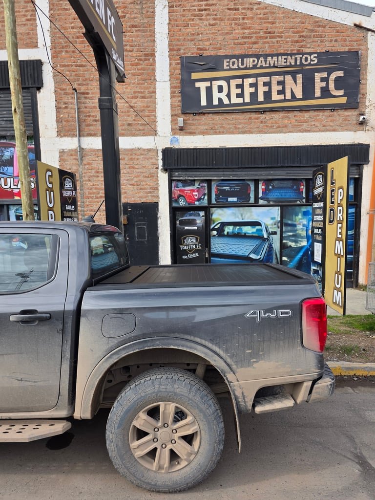 Silver pickup truck parked outside Treffen FC auto parts store with brick storefront and window displays