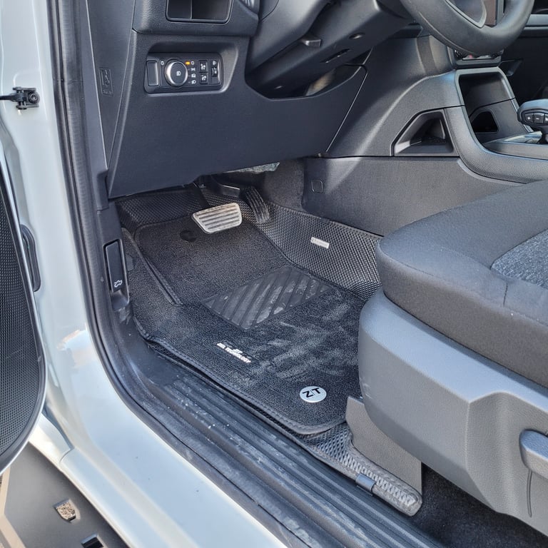 Car interior showing drivers side floor with black rubber floor mats, steering wheel, and dashboard controls visible
