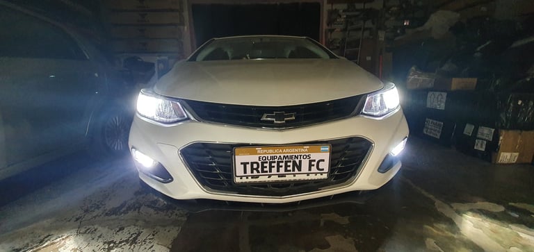 White Chevrolet car with headlights on, parked indoors with custom license plate reading TREFFEN FC