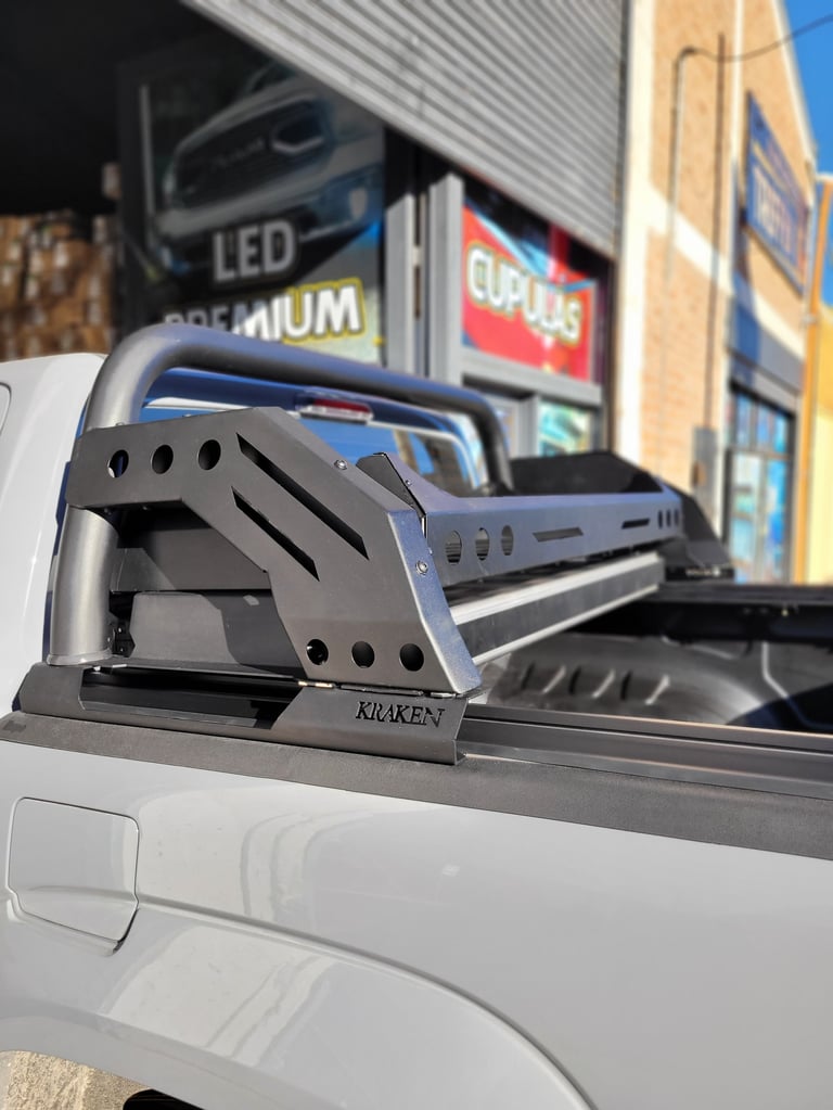 Black Karken truck bed rack mounted on white pickup truck bed with auto shop storefront in background