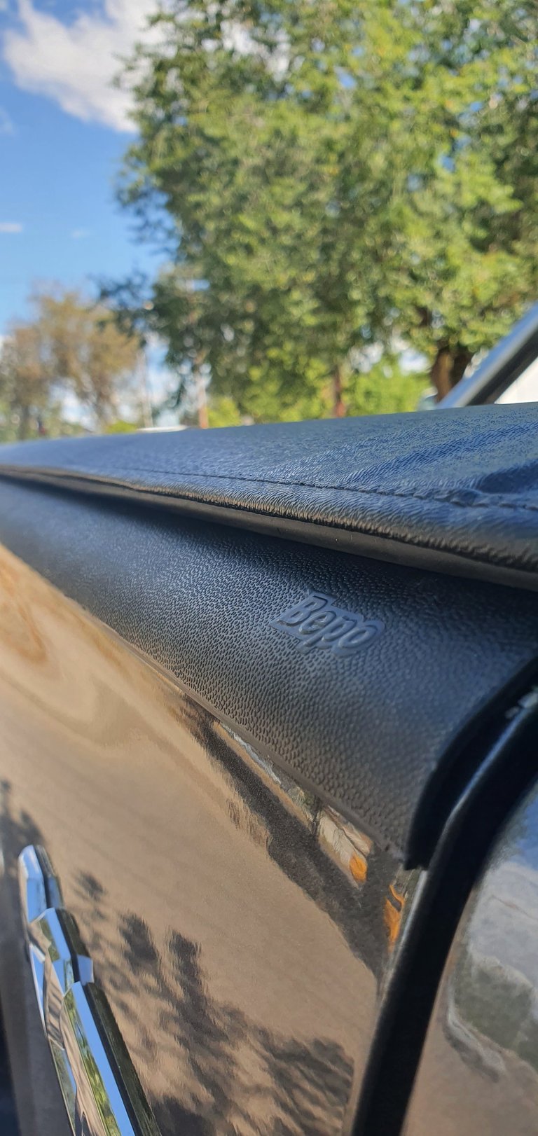 Close-up of a truck bed cover with trees and blue sky visible in the background