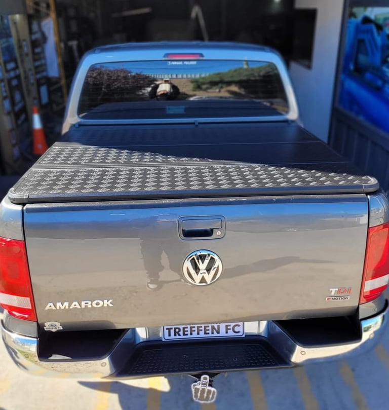 Rear view of a blue Volkswagen Amarok pickup truck with tonneau cover and custom license plate