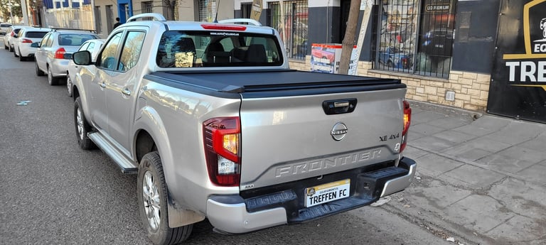 White Nissan pickup truck parked on urban street with tonneau cover and taillights visible