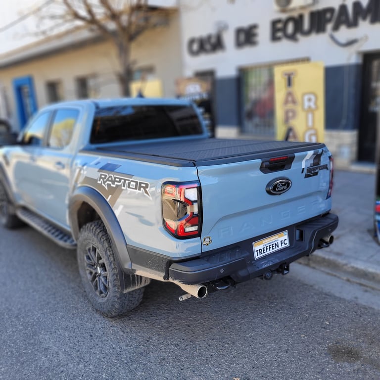 Blue Ford Raptor pickup truck parked on street with tonneau cover and black bumper