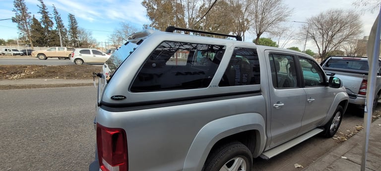 Silver pickup truck with camper shell in parking lot surrounded by bare trees