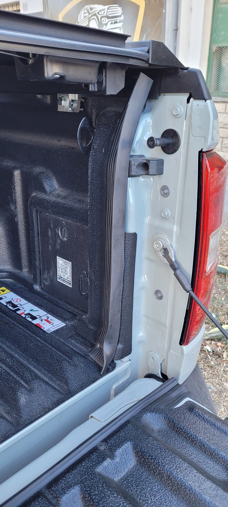 Open truck bed showing black bed liner, white tailgate with red brake light, and door latch mechanism