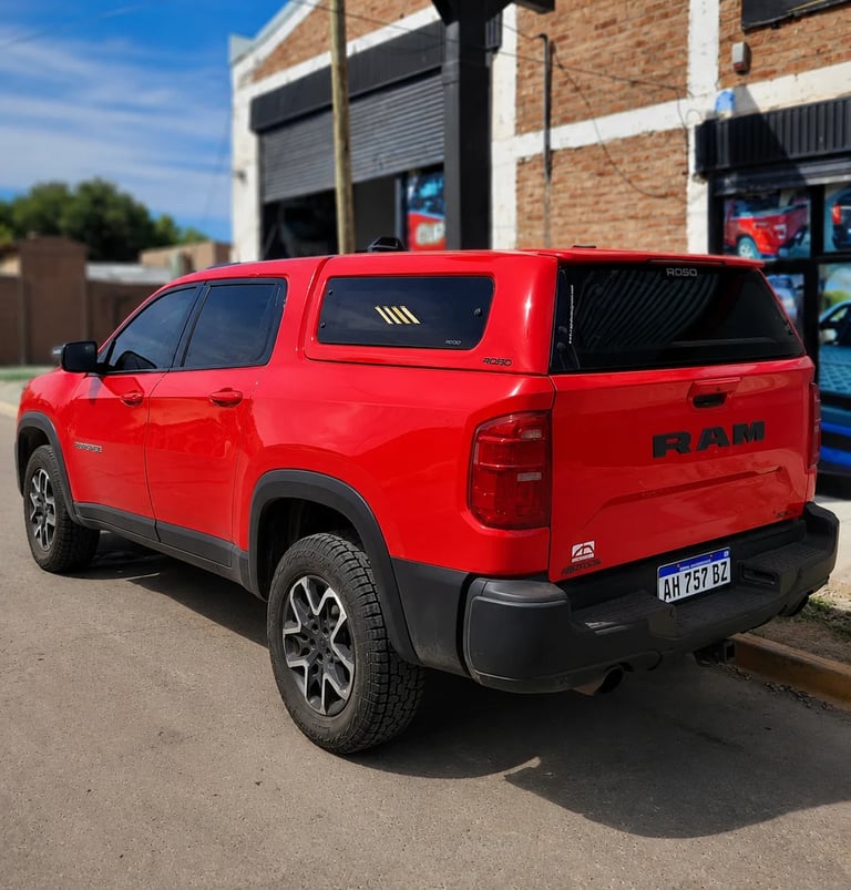 Red RAM pickup truck parked in front of a brick building, viewed from the rear three-quarter angle
