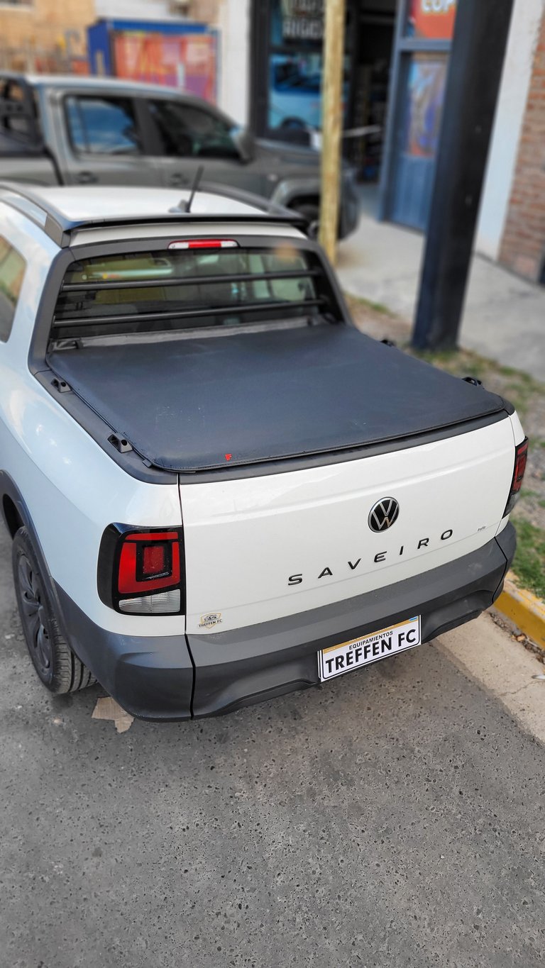 White Volkswagen Saveiro pickup truck with tonneau cover and red taillights, parked on a street