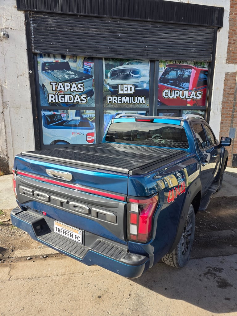 Blue pickup truck with tonneau cover parked in front of auto parts shop displaying truck accessories