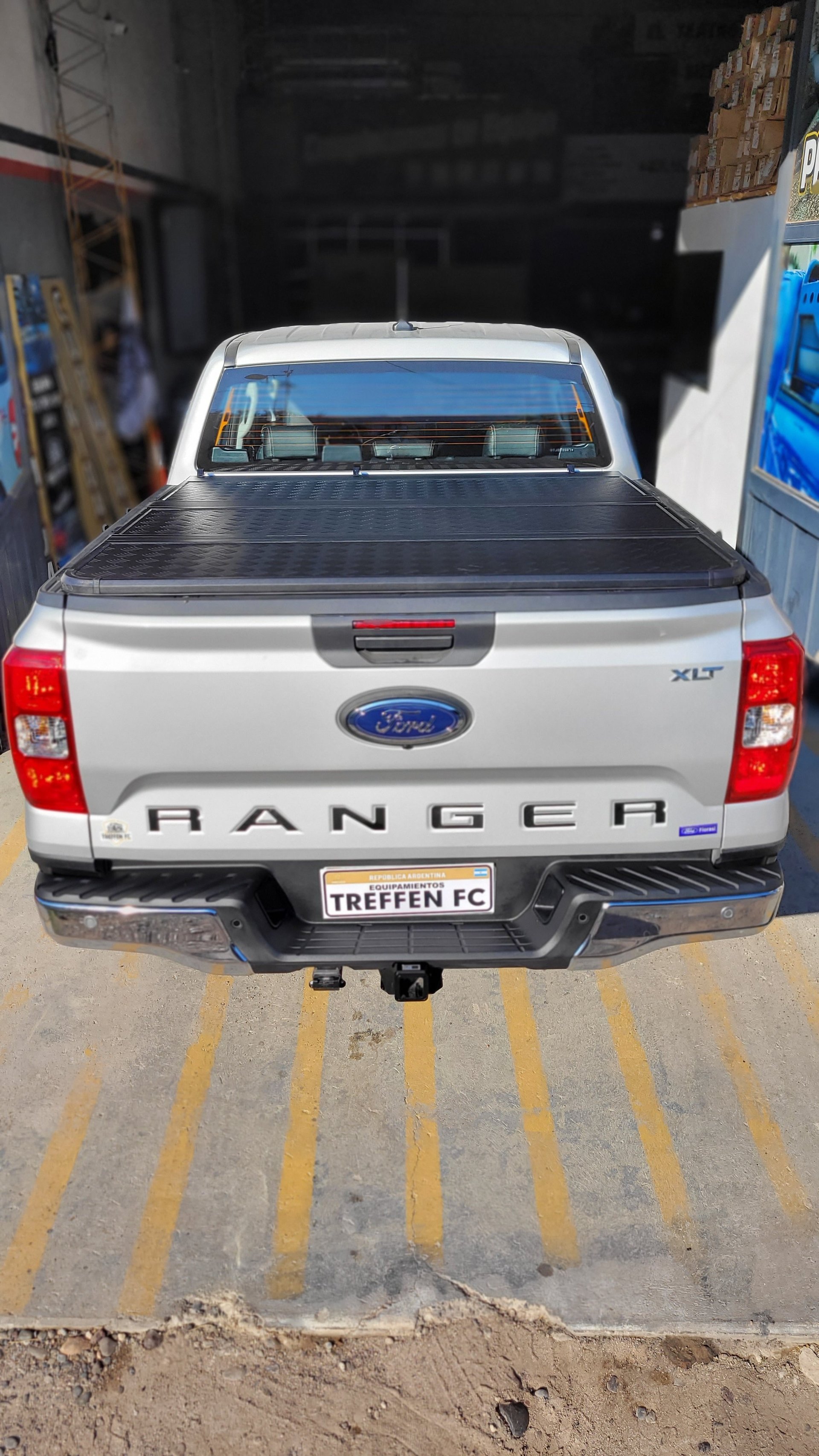 Rear view of a white Ford Ranger pickup truck with tonneau cover and custom license plate in a parking garage