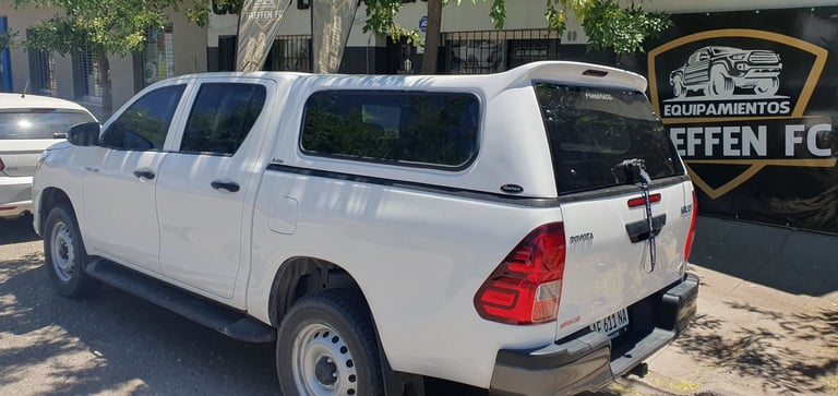 White pickup truck with canopy parked in lot with buildings and signage visible in background