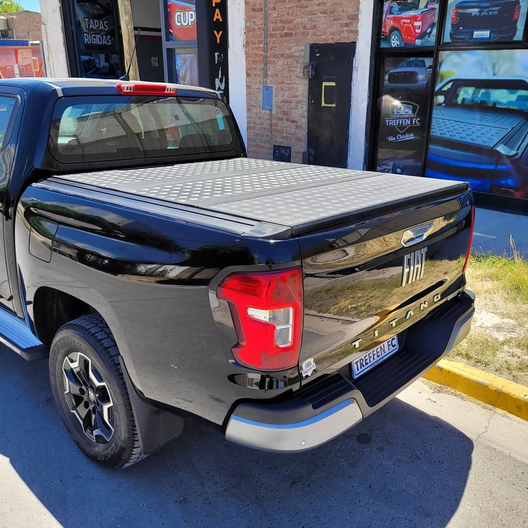 Blue and silver pickup truck with tonneau cover and red taillight parked outside storefront