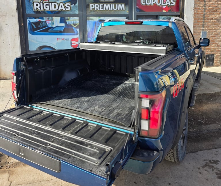 Blue pickup truck with open bed and tonneau cover displayed at an auto shop