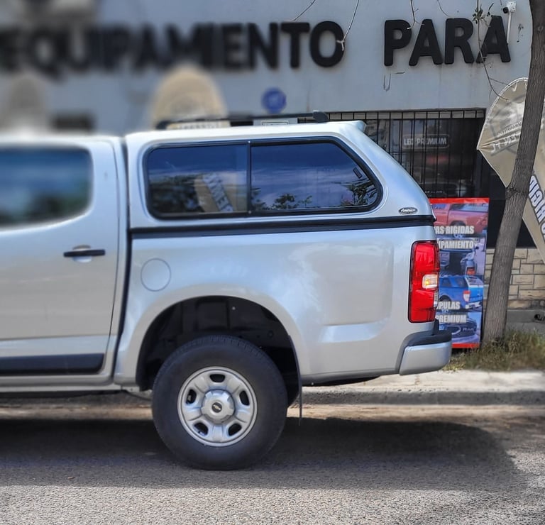 White pickup truck with camper shell parked in front of a building with Portuguese text signage