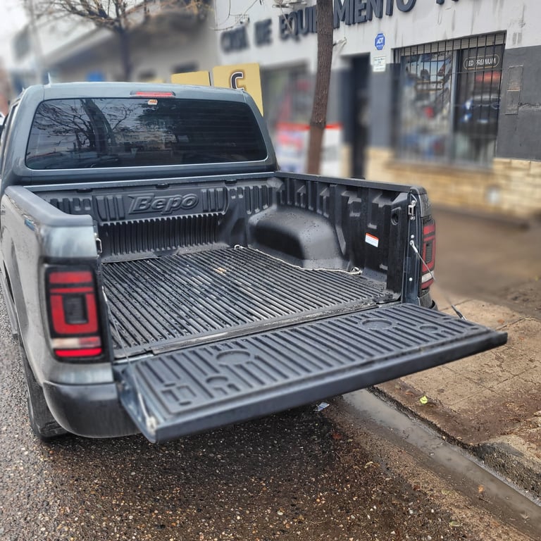 White pickup truck with open bed showing metal tailgate down in an urban street setting