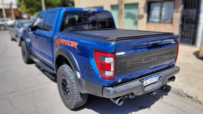 Blue Ford F-150 pickup truck with tonneau cover and dual exhaust, parked on a street near brick buildings