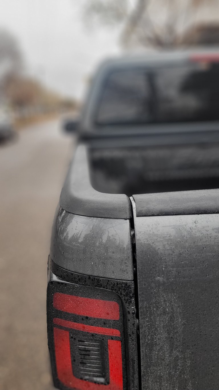 Close-up of a dirty pickup truck tailgate and red brake light, with another vehicle blurred in the background