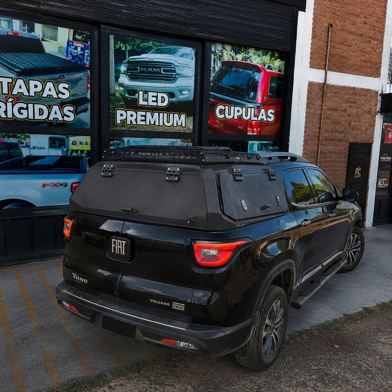 Black Fiat Toro SUV parked outside auto shop with illuminated storefront signs behind it