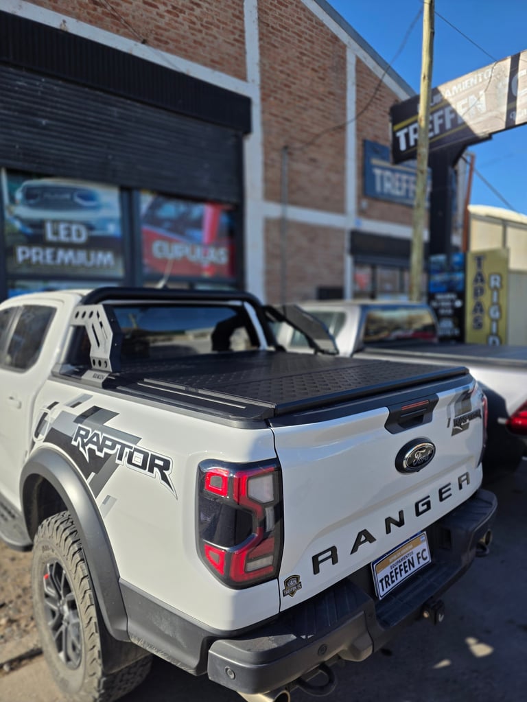 White Ford Ranger Raptor pickup truck with tonneau cover parked in front of brick automotive shop building