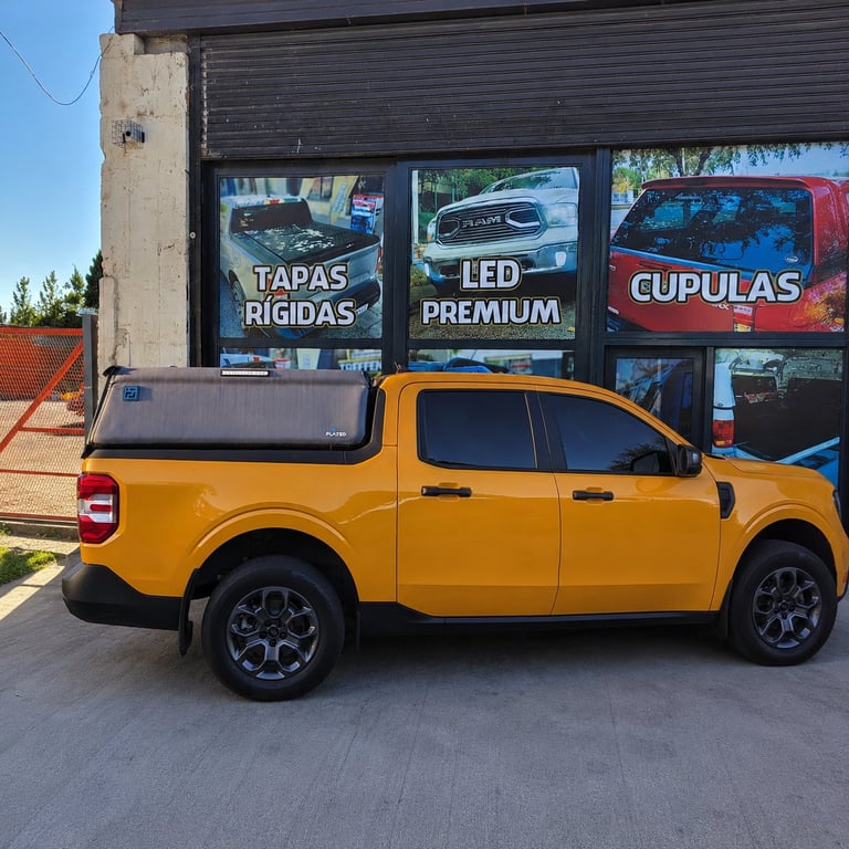 Yellow pickup truck with tonneau cover parked in front of an automotive shop with Spanish signage