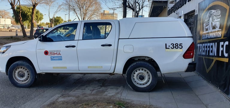 White Toyota pickup truck with utility canopy parked on street next to sports facility