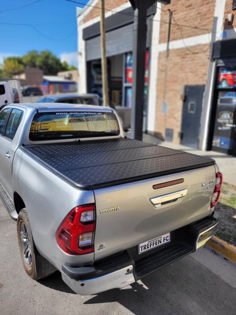 White Toyota pickup truck with black tonneau cover parked at a service facility on a sunny day