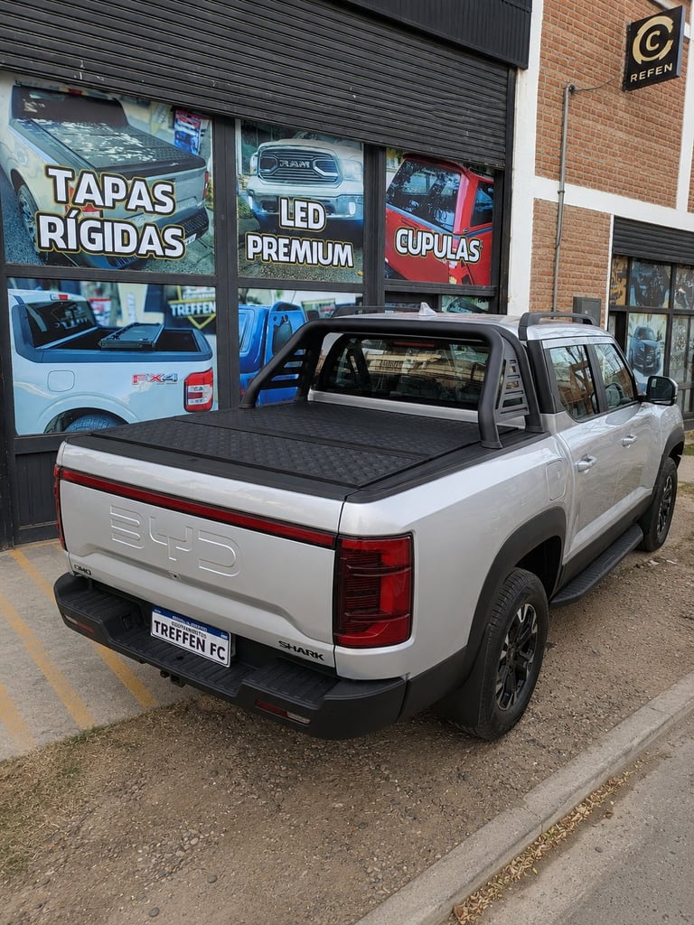 White pickup truck with tonneau cover displayed outside an auto accessories shop with promotional signage