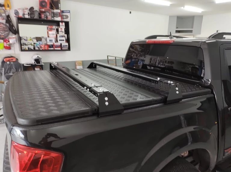 Black pickup truck with open tonneau cover in a garage workshop with tools and bulletin board visible in background