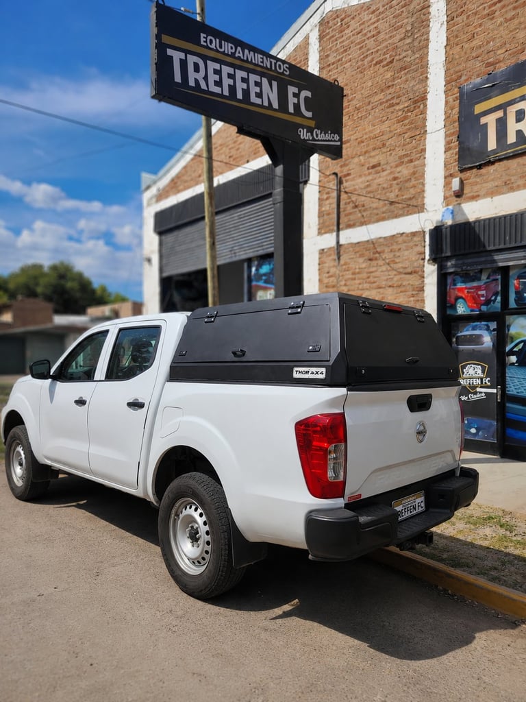 White pickup truck with black tonneau cover parked outside Treffen FC sports equipment store under blue sky