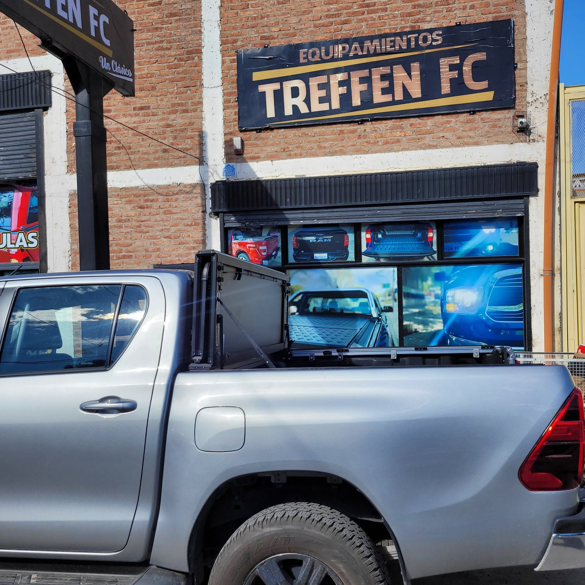 Silver pickup truck parked in front of Treffen FC sports equipment shop with blue storefront windows