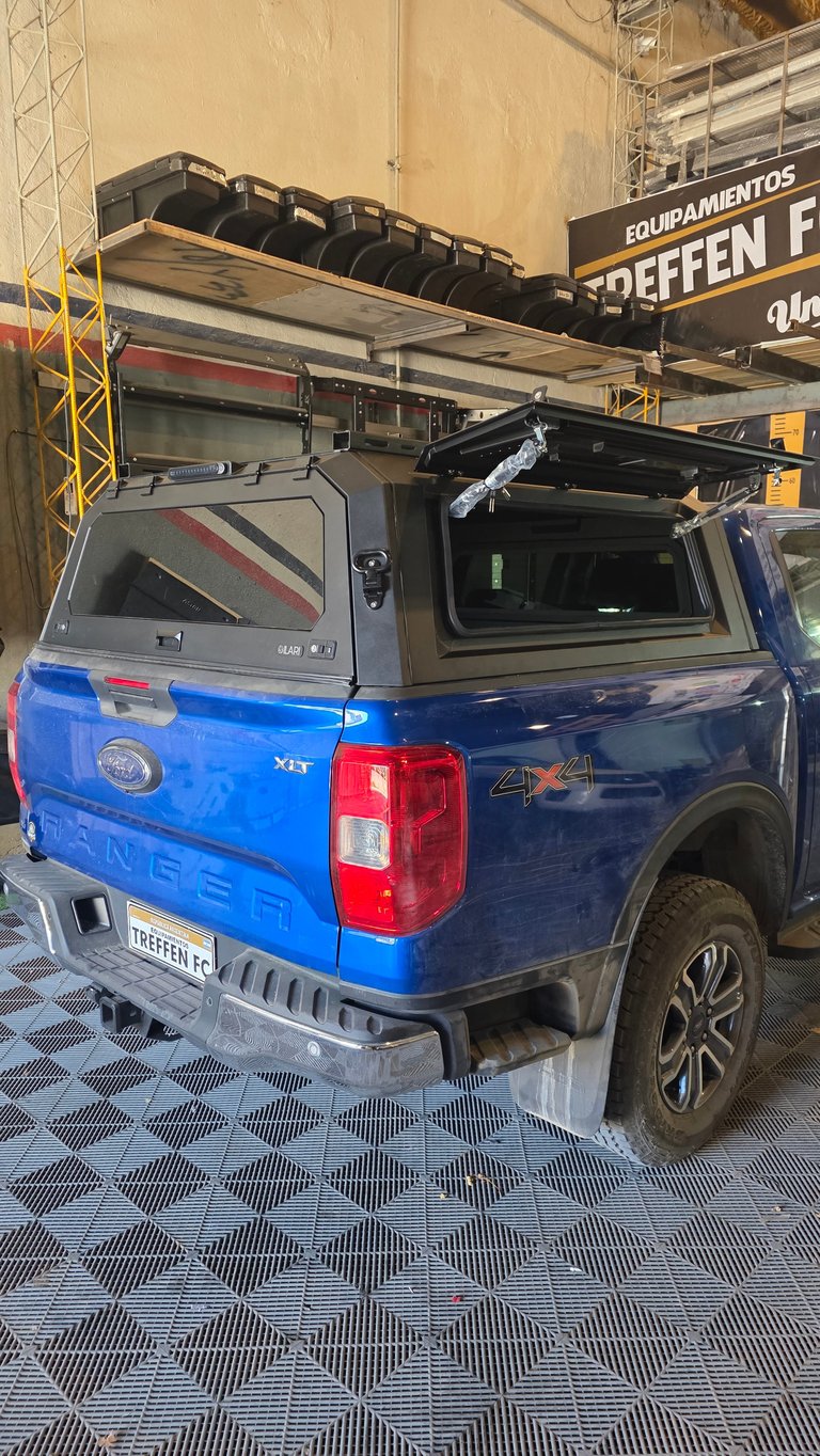 Blue pickup truck with open tonneau cover and roof rack mounted in industrial warehouse setting
