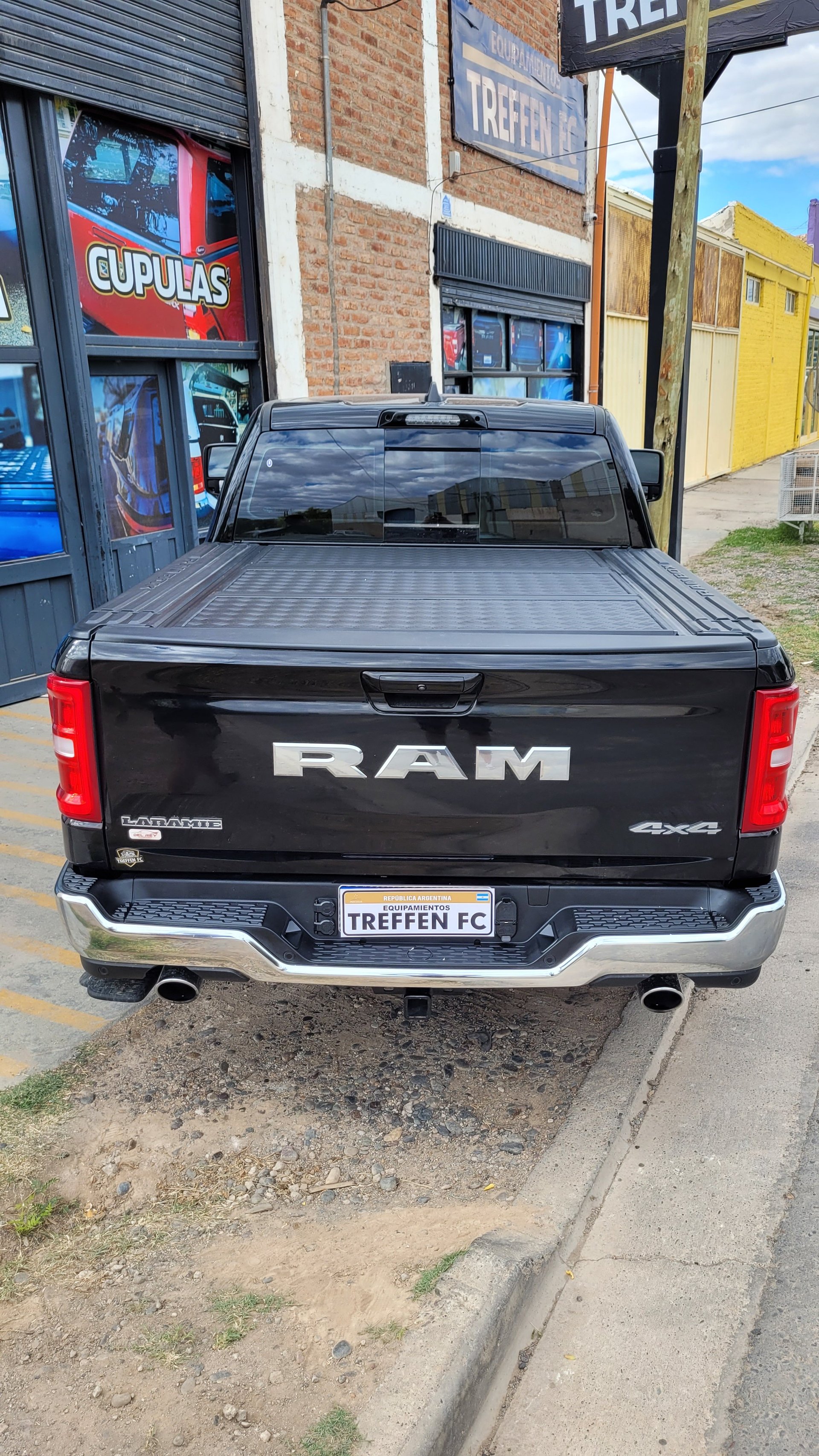 Black RAM pickup truck with tonneau cover parked on street with brick buildings in background