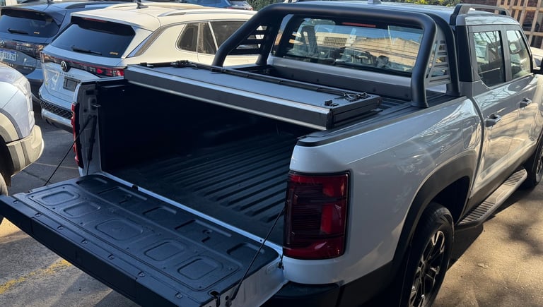 Silver pickup truck with open bed and tonneau cover in parking lot, showing cargo area