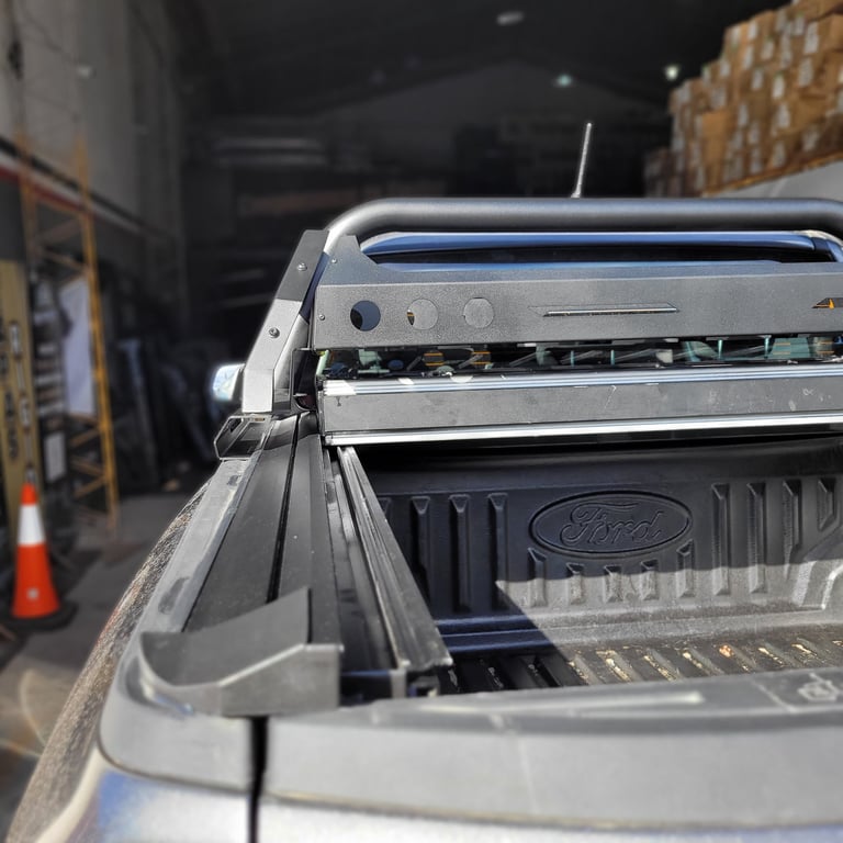 Close-up of a silver Ford pickup truck bed with tonneau cover partially open in a warehouse or parking area