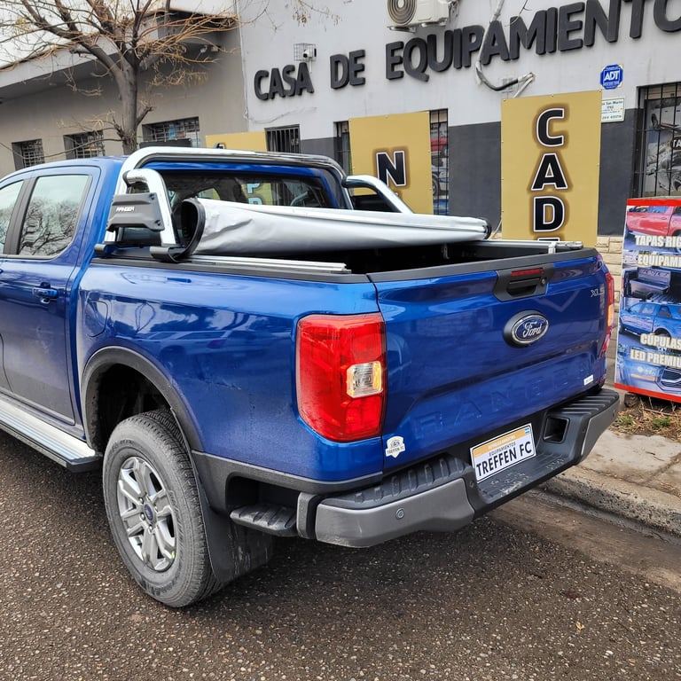 Blue Ford pickup truck with black tonneau cover parked outside a building with Casa de Equipamentos signage