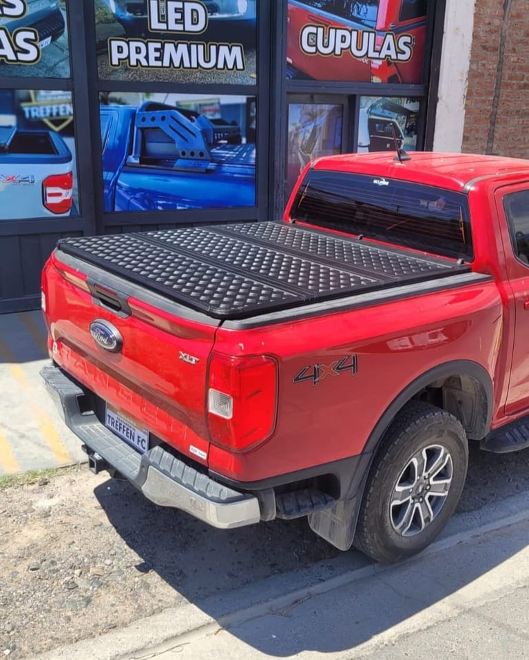 Red Ford pickup truck with black tonneau cover displayed outside auto parts shop with LED lighting signage